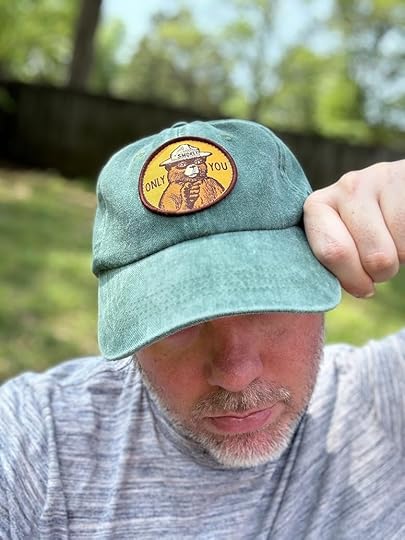 A person wearing a green cap with a Smokey Bear patch that reads
