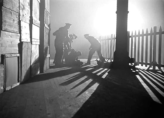 Three men beat a fourth in the spotlit darkness in