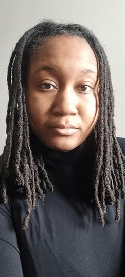 Headshot of a Black woman author with dreads, neutral expression looking into the camera, wearing a black top, against a plain wall background.