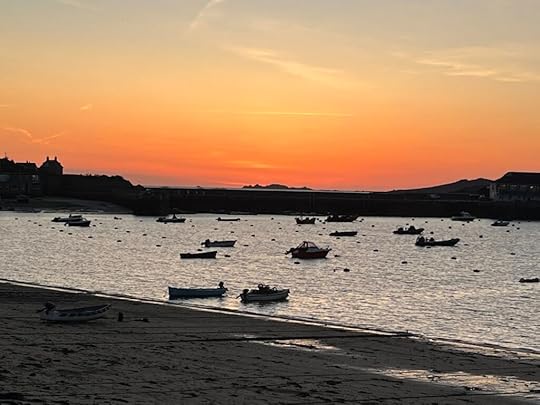 Red sky of sunset over the Hughtown bay, with dark shapes of boats visible on the calm, grey sea. 