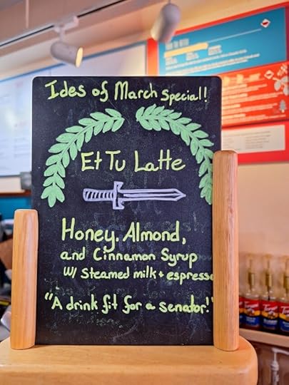 A chalkboard sign in a coffee shop with a drawing of a laurel wreath bracketing the words: "Ides of March special! Et Tu Latte - Honey, almond, and cinnamon syrups with steamed milk and espresso"