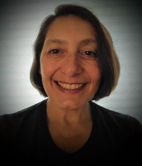 A portrait of author N. E. White. An older Caucasian woman smiles confidently. She has a dark blouse and chin length hair.