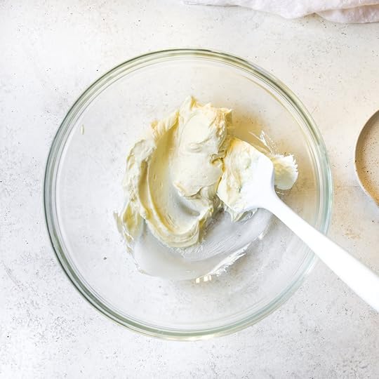 Softened butter and cream cheese being creamed together in a clear glass bowl with a white spatula, an essential first step for a rich chocolate buttercream frosting recipe.