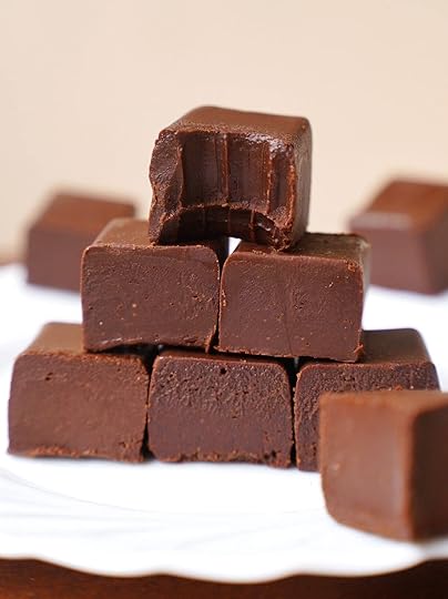 A stack of smooth, square-shaped chocolate fudge pieces, with one piece on top showing a bite taken out of it