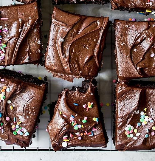 Top-down view of delectable chocolate dessert bars topped with luscious dark chocolate icing, brightly colored sprinkles, and a sprinkle of gourmet sea salt, arranged on a cooling rack, with one piece showing a bite taken, highlighting a perfect homemade sweet treat.