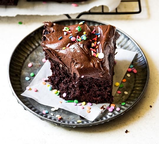 Single slice of moist dark chocolate cake beautifully topped with generous swirls of homemade chocolate frosting and festive rainbow confetti sprinkles, presented on a rustic metal serving plate, perfect for an individual sweet treat or birthday celebration