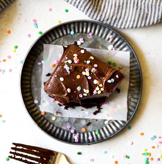 A delectable slice of homemade chocolate sheet cake generously topped with rich chocolate buttercream frosting and vibrant rainbow sprinkles, served on a rustic fluted metal plate with a chocolate-smeared fork, embodying a perfect party dessert or easy sweet treat recipe.