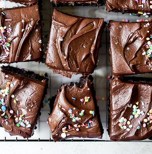 Overhead shot of moist, fudgy chocolate dessert bars generously topped with a rich, velvety chocolate frosting, some decorated with cheerful multi-colored confetti sprinkles, others with glistening sea salt flakes, arranged on a wire cooling rack, perfect for a delightful homemade treat or celebration.