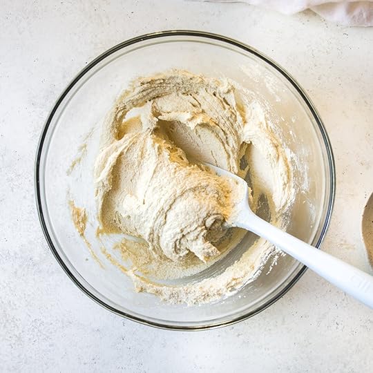 Creamed butter and sugars being mixed in a clear glass bowl with a white spatula, an early step in preparing the wet ingredients for a rich homemade chocolate sheet cake recipe.