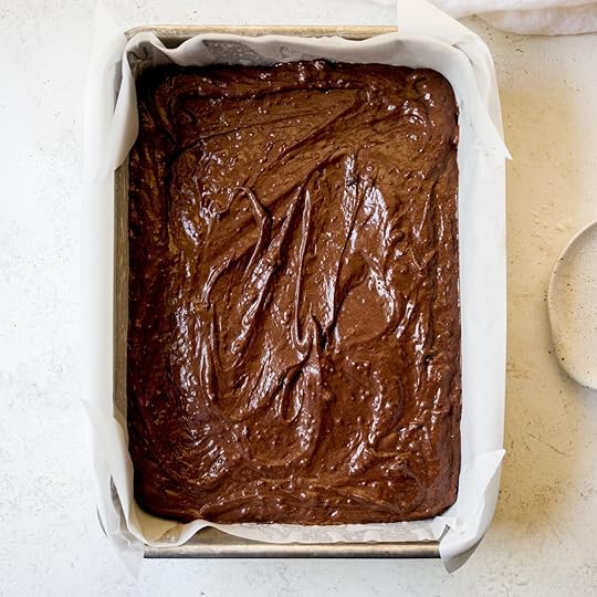 Smooth, glossy chocolate sheet cake batter evenly spread in a parchment paper-lined rectangular baking pan, ready for baking in a homemade chocolate cake recipe.