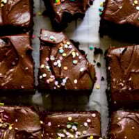 Overhead view of homemade chocolate sheet cake squares generously frosted with rich chocolate buttercream, adorned with vibrant rainbow sprinkles and a touch of flaky sea salt, perfect for a festive party dessert.