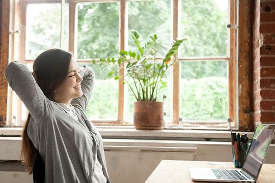 Happy woman sitting at a desk with a laptop stretching her arms. If perfectionism and ADHD are keeping you stuck in a loop or stress or burnout find positive ways to cope with perfectionism treatment in Houston, TX.