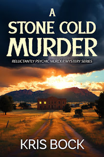 A book cover shows a dirt road with prairie grasses on either side. It leads toward a two-story building that looks ominous with only two windows lit up. Behind the building, the sun sets over a mountain. Dramatic clouds billow up, getting darker behind the book title: A Stone Cold Murder: The Reluctant Psychic Murder Mystery series by Kris Bock.