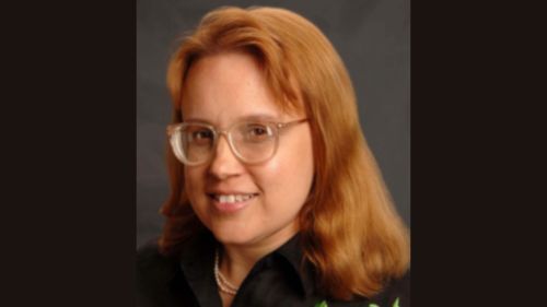A portrait of author Rosemary Jones. A Caucasian woman smiles confidently. She has shoulder length red hair and eye glasses.