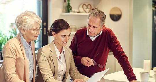 Two people stand beside a person in a business suit who is sitting and holding a pen and piece of paper.