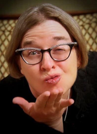 Portrait of author Jennifer Stevenson. A caucasian woman winks as she blows you a kiss. Her hair is light brown and she wears rhinestone eye glasses.
