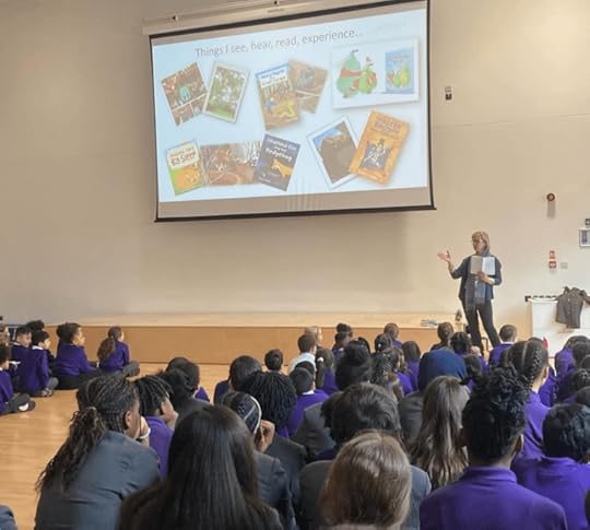 Image of Karen Inglis children's author talking to an assembly hall of school pupils. A screen on the wall shows book titles and photos relating to the stories.
