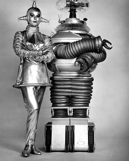 A vintage black and white photograph featuring a humanoid robot and a woman dressed in a metallic, futuristic outfit.