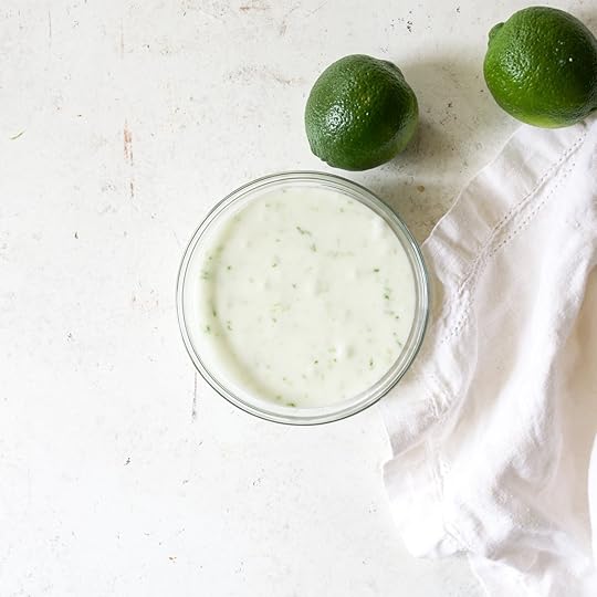 Overhead shot of a bowl of creamy, finished lime glaze with whole limes nearby