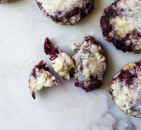 Overhead close-up of tender,sugar-dusted blackberry sconeson a marble surface, one scone brokento reveal its fluffy, moist interior andvibrant purple berries, homemadefruit scone recipe from DisplacedHousewife.