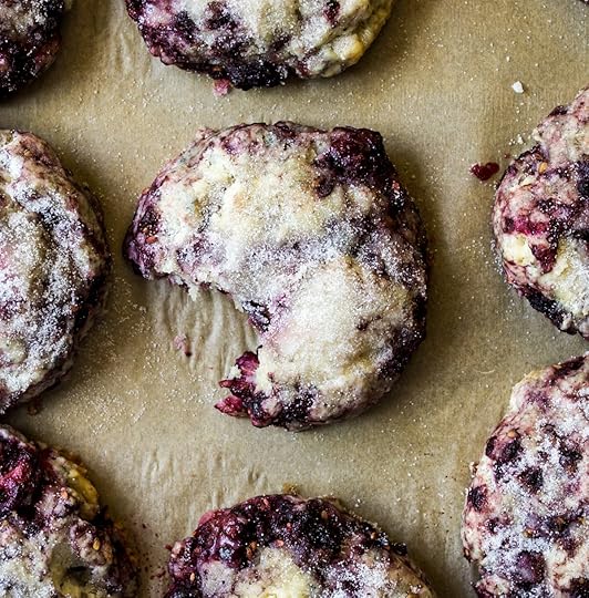 Overhead view of freshly bakedblackberry scones with a sparkling sugar topon light brown parchment paper, one sconein the center has a bite taken out, revealingthe juicy purple berries and moist interior,homemade fruit scone recipe from DisplacedHousewife.