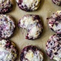 Overhead shot of freshly baked blackberry scones with a sparkling sugar top on parchment paper, one scone with a bite taken out, revealing juicy berries and tender crumb, homemade fruit scone recipe from DisplacedHousewife.