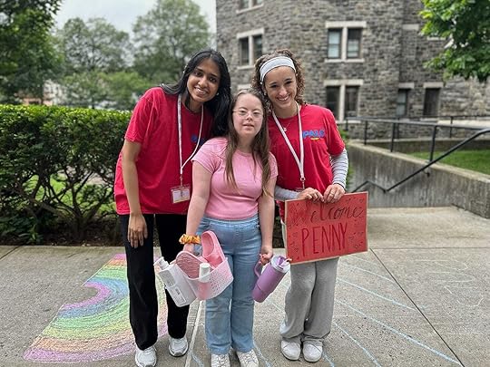 Penny and two members of a welcome team smile outdoors in front of a stone building. The welcome team is wearing matching red 