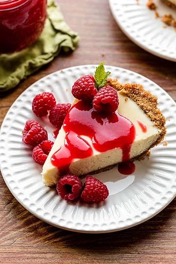 cheesecake slice on white plate with raspberry sauce and fresh raspberries on top.