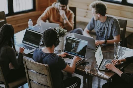 A group of people using computers at a table. What are you doing and why are you doing it?