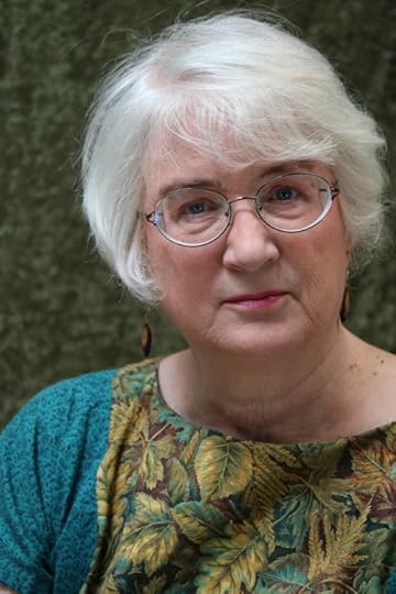 Portrait of author Irene Radford. A Caucasian woman with silver hair and eye glasses. Her dress is blue, with gold and green leaves on the front.