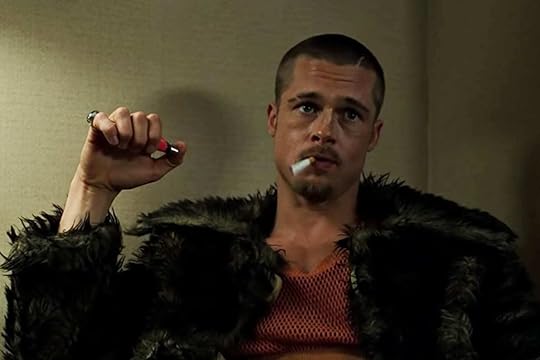 Brad Pitt holds a red lighter. His head is shaved and he's wearing a fur coat and a red mesh tank top. Still from
