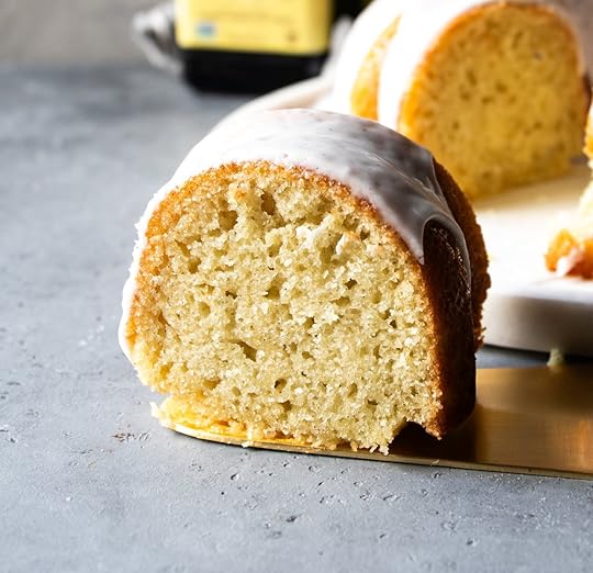 Close-up of a slice of moist vanilla bundt cake with white glaze and visible vanilla bean flecks, on a gold cake server