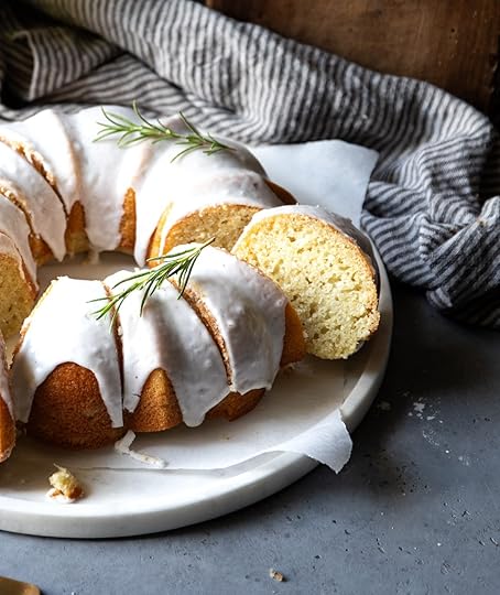 A beautifully sliced vanilla bundt cake with white glaze and fresh rosemary sprigs on a white platter, ready to serve.