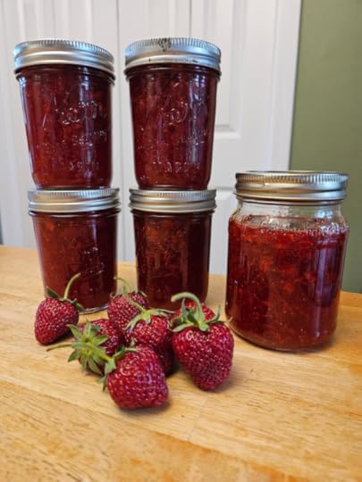 Jars of strawberry jam, stacked on top of each other, with a few fresh strawberries in front.