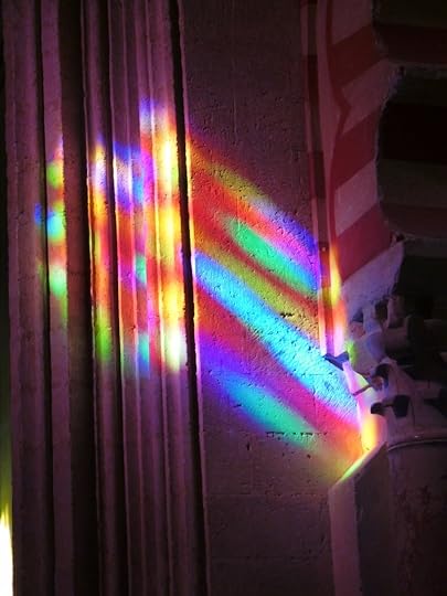 Colorful light reflections casting patterns on a textured wall, with columns and architectural details visible.