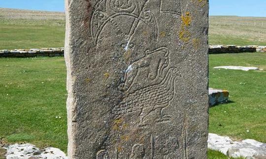 a carved stone stands upright in a green field with the ocean in the distance. Pictish symbols decorate the front