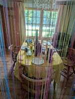 Dining table behind a string curtain, before a gold draperied window