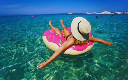 girl in a pink inner tube in the ocean with a hat on