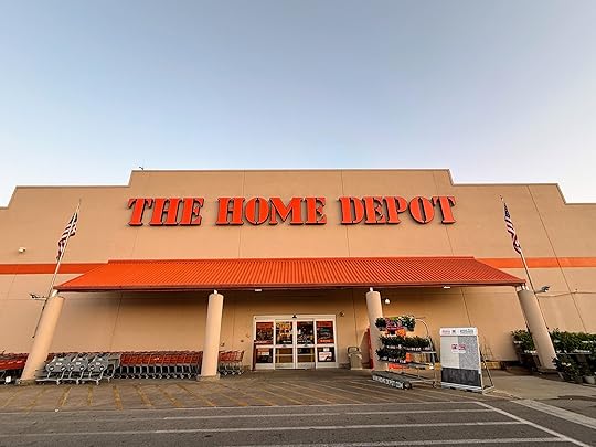The image shows the exterior of a Home Depot store. The building has a beige facade with a large orange sign displaying