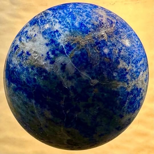 A polished sphere of lapis lazuli with cream and light brown inclusions that make it look like the planet earth spinning in front of a buff-coloured padded envelope