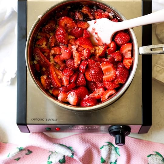  A pink spatula is seen stirring vibrant chopped strawberries, white sugar, and diced apple in a stainless steel pot on a hot plate, beginning the cooking process for homemade, no-pectin strawberry jam.