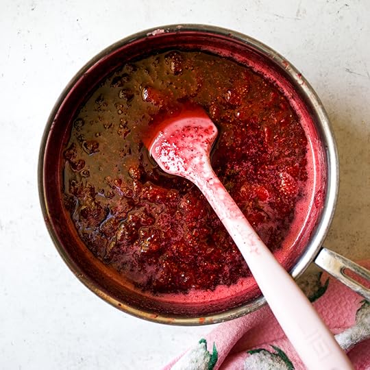 A vibrant, thick mixture of cooked strawberries, sugar, and apple in a stainless steel pot, with a pink spatula still resting in the rich red homemade jam, indicating it's nearly finished cooking.
