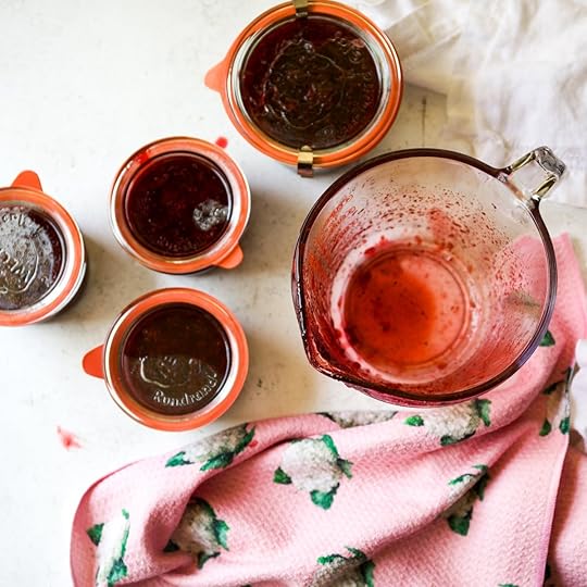A birds-eye view captures several glass jars filled with homemade strawberry freezer jam, their orange clamps visible, alongside an empty, jam-splattered measuring cup and a pink towel, showcasing the successful bottling of fresh, no-pectin jam.