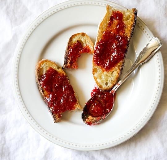 A white plate holds several pieces of toasted bread slathered with vibrant homemade strawberry freezer jam, with a spoon still glistening with jam next to them, showcasing a delicious serving suggestion.
