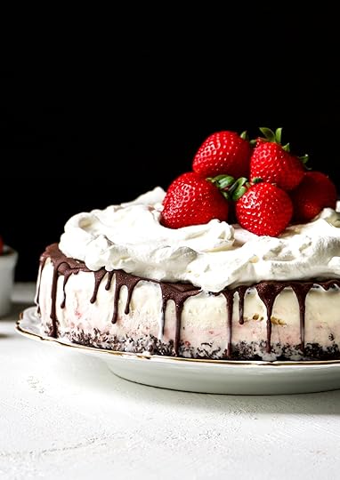 Homemade Neapolitan ice cream cake with a chocolate crust, layers of strawberry and vanilla ice cream, draped in chocolate ganache, and topped with fresh whipped cream and ripe strawberries.