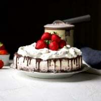Easy Neapolitan ice cream cake with chocolate cookie crust, strawberry and vanilla ice cream layers, chocolate ganache drip, whipped cream, and fresh strawberries on top.