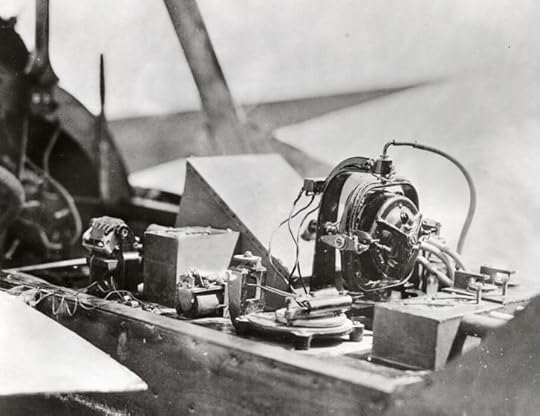 A close-up black-and-white photo shows a mess of wires and air bellows that comprise the engine and flight system of an early drone biplane.