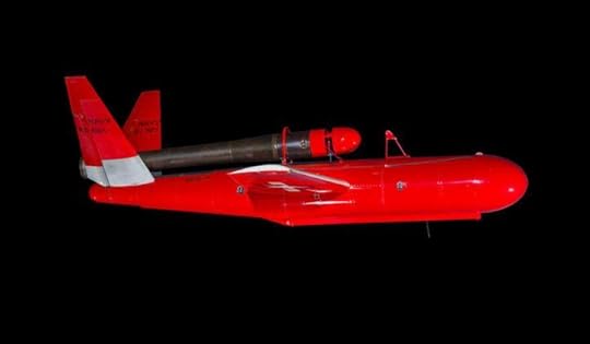 A bright red, small pilotless aircraft—resembling a missile with wings—has a large grey metal tube mounted on its back.