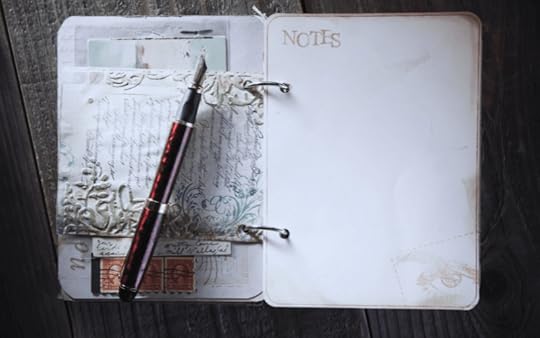 A white notebook on a black desk with a black pen