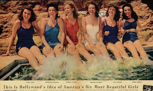 Six young women in swim suits kick their legs in the water while smiling and laughing, all looking just off camera. It's a bright day. A reddish outcropping of rocks, perhaps forming a low hill, are just behind them.